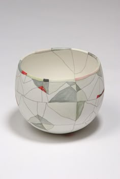 a white bowl with red and green designs on the rim, sitting in front of a gray background