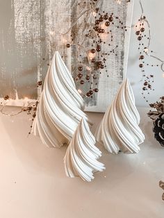 three white vases sitting on top of a table next to a christmas tree and pine cones