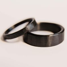 two black wedding bands sitting on top of each other in front of a white background