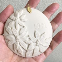 a hand holding a white ceramic ornament with flowers on it's side