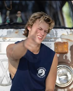 a woman pointing at the camera in front of an old van with her eyes closed