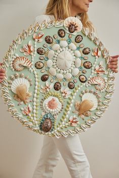 a woman is holding a large piece of art made out of shells and seashells