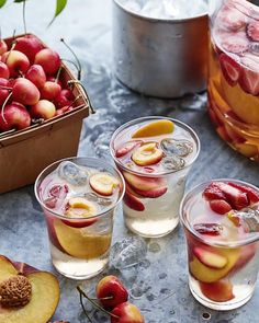 two glasses filled with ice and cherries next to some jars full of fruit on a table