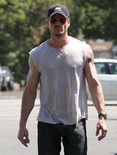 a man walking across a parking lot holding onto a skateboard with one hand on his hip