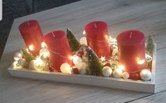 some red candles are sitting on a wooden tray with christmas decorations and lights around them