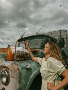 a woman standing next to an old green truck with a basket on the hood and holding something in her hand