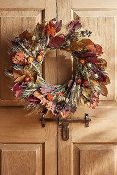 a wreath on the front door of a house with leaves and flowers hanging from it