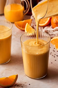 an orange juice being poured into two glasses