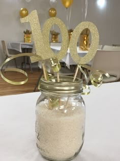 a mason jar filled with white sand and some gold decorations on top of a table