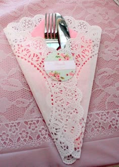 a pink table cloth with white doily and silverware on it, sitting next to a fork and knife