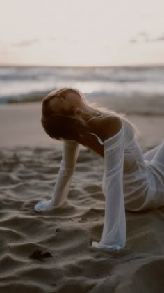 a woman laying on top of a sandy beach next to the ocean with her legs in the air