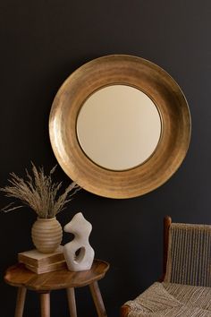 a round mirror sitting on top of a wooden table next to a vase and chair