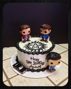 two small figurines sitting on top of a white cake with black frosting