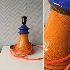 an orange and blue vase sitting on top of a white table next to a lamp