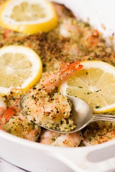 a bowl filled with shrimp and lemons on top of a white tablecloth next to a spoon