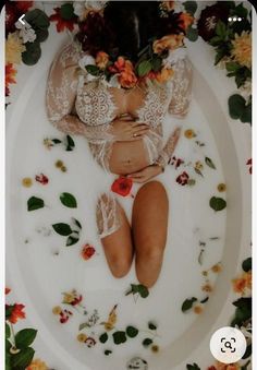 a woman laying in a bath with flowers all around her and wearing a lacy top