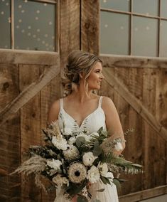 a woman holding a bouquet of flowers in front of a barn