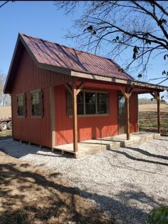 a small red building sitting in the middle of a dirt field next to a tree