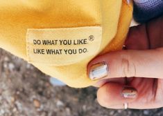 a person's hand holding onto a yellow shirt with writing on it that says do what you like like what you do