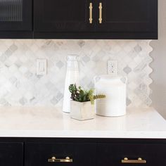 two white vases sitting on top of a counter next to a black cabinet with gold handles