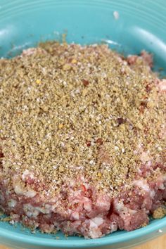 a blue bowl filled with meat covered in seasoning on top of a wooden table