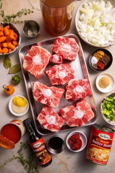 raw meats and vegetables on a tray next to a pitcher of beer, seasonings, spices, and sauces