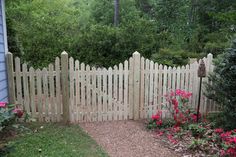 a white picket fence with pink flowers in the foreground and blue house behind it