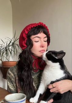 a woman in a red hat holding a black and white cat while sitting at a table