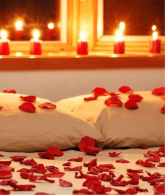 two pillows on a bed with rose petals and candles in the window sill behind them