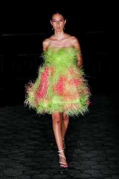 a woman is walking down the runway in a green dress with pink and yellow feathers