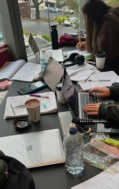 two people sitting at a table with laptops and notebooks on top of them