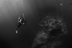 a person swimming in the water near a rock formation with other rocks and debris around them