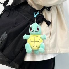 a small stuffed turtle is hanging from a back pack pocket in someone's hand