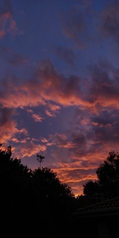 the sky is pink and purple as it sets over trees in front of a building