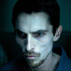 a man with white makeup and dark hair looks at the camera while wearing a blue shirt