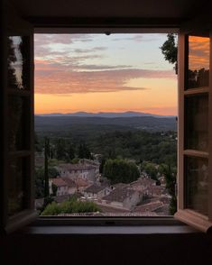 an open window with the view of a town and mountains in the distance at sunset