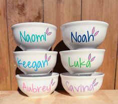 four bowls with names painted on them sitting on a wooden table top next to a wood wall