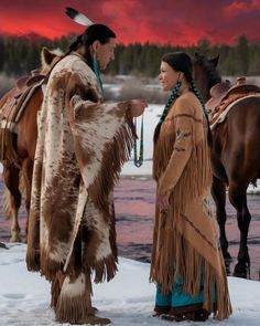 two native americans standing next to each other in the snow with horses and sunset behind them