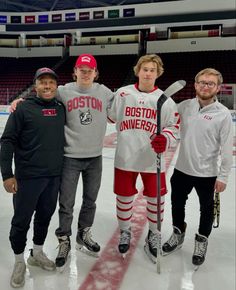 three men standing on an ice rink holding hockey sticks and posing for the camera with one man wearing boston university's jersey