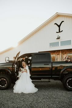 a woman in a wedding dress standing next to a black truck with the door open