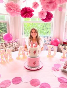 a woman sitting at a table with a cake in front of her and pink decorations