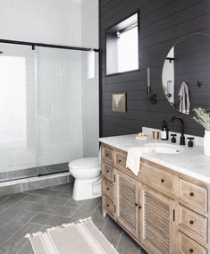 a white toilet sitting next to a bathroom sink under a mirror on top of a wooden cabinet