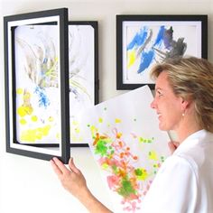 a person holding up two framed paintings on the wall with their hands in front of them