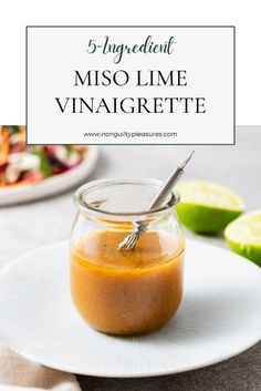 a small glass jar filled with sauce sitting on top of a white plate next to sliced limes