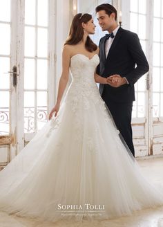 a man and woman standing next to each other in front of an open door wearing wedding dresses