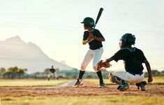 two baseball players in black shirts and white pants are playing baseball on a field with mountains in the background