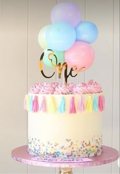 a birthday cake with balloons and the number one on top is decorated in pastel colors