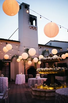 an outdoor wedding reception with paper lanterns and table linens on the outside, lit up by string lights