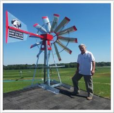 a man standing next to a red and white windmill on top of a roof in front of a field