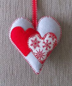 two red and white hearts hanging from a red ribbon on a gray surface with snowflakes